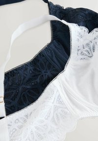 Navyblauer und weißer BH mit Spitzenverzierungen, gepunkteter Textur, verstellbaren Trägern und feinen gewellten Kanten.