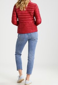 Rød puffjakke med vandret syninger, parret med lyseblå højtaljede jeans og lyseblå sneakers. Simpelt design, ingen synlige logoer.