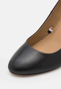 Escarpin en cuir noir à finition lisse, bout pointu et design minimaliste. Intérieur doté d'une doublure beige clair et de détails subtils de couture.