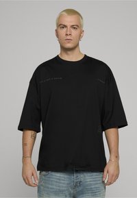 Černé oversized tričko s krátkými rukávy. Má grafický nápis v tmavě šedé barvě, vyrobené z měkké látky. Ležérní design, kulatý výstřih.