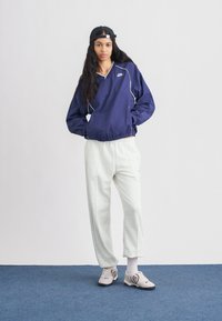 Ναυτικό ανοιξιάτικο μπουφάν με λευκές λεπτομέρειες, ελαστική μέση; γκρι φόρμα; μπεζ αθλητικά παπούτσια με μαύρες λεπτομέρειες; άτομο που φοράει μαύρο καπέλο.