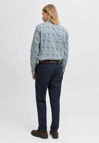 Camicia button-up azzurra chiara con motivo floreale, abbinata a pantaloni scuri. Presenta una vestibilità dritta e maniche lunghe. Cintura e scarpe marroni.