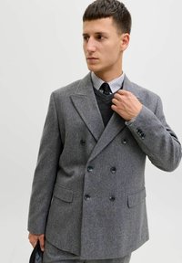 Hall hall kahe rea nööbiga jakk, mis on valmistatud tekstureeritud villast, kus on suured mustad nupud, sisselõigatud kraed ja küljetaskud, kantud tumeda kampsuni peal.