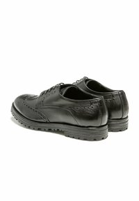Chaussures habillées en cuir noir avec des détails en brogue, un design à lacets et une semelle en caoutchouc texturée, présentées de dos et sous un angle.