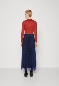 Un top roșu cu mâneci lungi, asortat cu o fustă maxi din tull albastră, cu un model, având talie plisată și un design stratificat. Pantofii cu platformă negri completează look-ul.