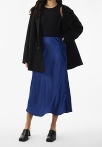 Svart kavaj, svart ärmlös topp, blå satäng midi-kjol, slät textur, ankellång, kombinerad med svarta klackskor med blockklack.