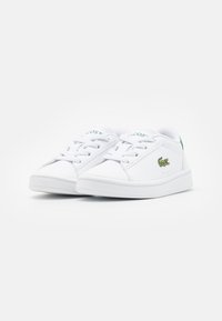 Sneakers bianchi con lacci e superficie liscia, dotate di un marchio verde sulla linguetta e di un logo a forma di coccodrillo verde sul lato.