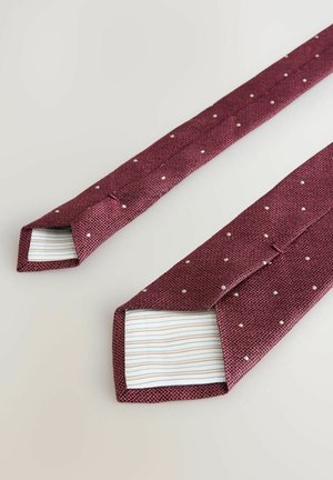 Cravate bordeaux en tissu texturé, ornée de petits points blancs et d'une doublure rayée à l'intérieur. Les extrémités sont pointues et légèrement plus larges.