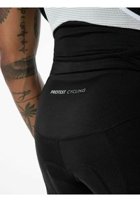 Schwarze Radsportshorts aus strukturiertem Material mit einem PROTEST CYCLING-Logo. Eine Nahaufnahme zeigt die Nähte und das figurbetonte Design.