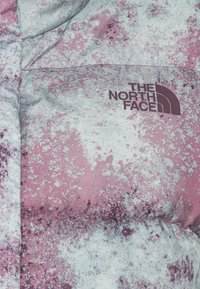 Doudoune avec un motif éclaboussé rose, blanc et violet, avec le logo « The North Face » sur la poitrine.