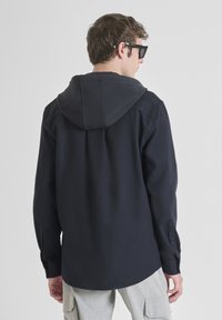 Mornarska dukserica s kapuljačom izrađena od pamuka, s dugim rukavima, manžetama na gumbe i opuštenim krojem s zakrivljenim rubom. Minimalistički dizajn.