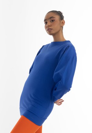 Königsblauer Oversize-Sweatshirt mit langen Ärmeln und gerippten Bündchen, kombiniert mit enganliegenden orangen Leggings. Weiches Material und lockere Passform.