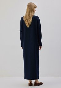 Robe bleu marine à manches longues avec une silhouette droite et un détail volanté sur la manche. Portée avec des ballerines à imprimé léopard marron.