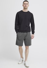 Sort sweatshirt, grå shorts med lomme og hvide sneakers. Afslappet pasform med ribbede manchetter og logo-detalje på shortsene. Rent design.
