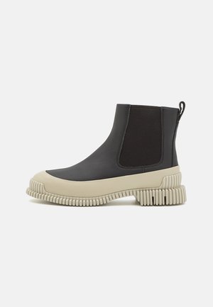 Botas Chelsea de cuero negro con suela de goma gruesa en color beige. Presenta paneles laterales elásticos y una suela texturizada y estriada para mayor agarre.