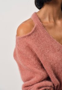 Roze oversized sweater gemaakt van zachte, gestructureerde stof, met een brede halslijn en off-shoulder ontwerp.