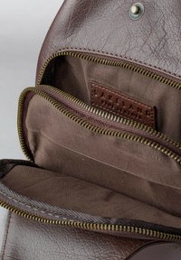 Brown leather bag with a textured exterior, featuring a dark brown fabric lining and a zippered compartment. Subtle brand label inside.