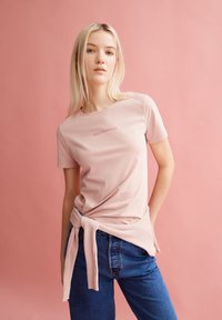 Lichtroze katoenen t-shirt met een ronde halslijn en korte mouwen, met de merknaam "ARMEDANGELS" in bijpassende kleur gedrukt.
