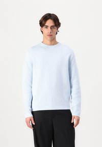 Light blue sweater in soft material with a crew neck, long sleeves, and a ribbed hem, paired with black trousers.