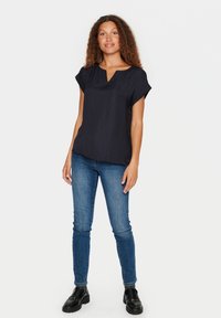Blusa navy a maniche corte con scollo a V, caratterizzata da un sottile motivo a pois. Abbinata a jeans skinny blu e mocassini neri chunky.
