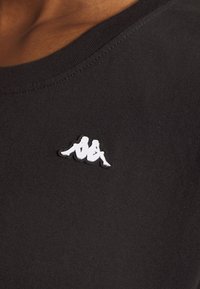 Czarny bawełniany t-shirt z okrągłym dekoltem, z białym haftowanym logo Kappa po lewej stronie, gładka faktura i krótkie rękawy.