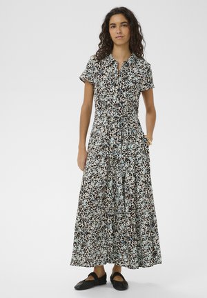 Femme portant une robe longueur cheville à manches courtes, boutonnée, avec un imprimé abstrait noir, blanc et bleu, et des chaussures plates noires.