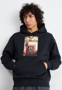 Sudadera negra con un gráfico frontal de una escena festiva de chimenea, con un bolsillo canguro y puños de canalé. Hecha de tela suave.