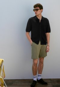 Black short-sleeve button-up shirt with a textured fabric, paired with beige shorts, white socks with black stripes, and black sneakers.