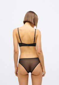 Črni komplet spodnjega perila zmodro čipkastim modrcem z nastavljivimi naramnicami in ujemajočimi se prozornimi hlačkami, oba s valovitimi robovi.