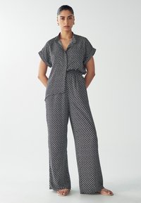 Jumpsuit a righe bianche e nere con scollatura a V, maniche corte e vita sul fianchi; design a gamba larga; morbida trama del tessuto.