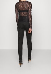 Czarna koronkowa bluzka z długim rękawem o dopasowanym kroju, nałożona na jednolity czarny pas. W zestawie z dopasowanymi czarnymi spodniami i szpilkami.