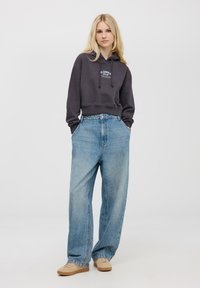 Czarna szara skrócona bluza z kapturem z białym napisem, w połączeniu z jasnoniebieskimi spodniami o szerokich nogawkach i beżowymi trampkami. Gładki materiał z luźnym fasonem.