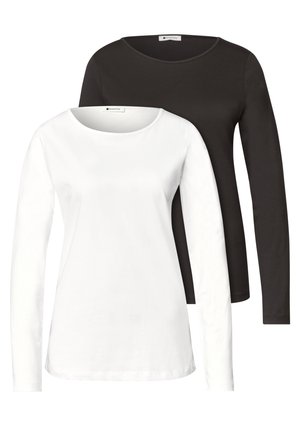 Deux femmes se tiennent côte à côte, portant des hauts décontractés et des jeans, l'une tient une pochette bordeaux, l'autre une veste bordeaux.