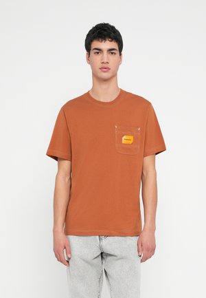 Katoenen T-shirt met korte mouwen in roestkleur, voorzien van een borstzakje met een geel label. Eenvoudige, losse pasvorm en nette stikdetails.