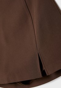 Jupe en tissu marron à texture lisse, avec un détail d'ourlet fendu. Design simple avec un bord net et sans quincaillerie visible.