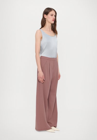 Top in satin azzurro chiaro abbinato a pantaloni a vita alta e gamba larga in rosa polveroso, caratterizzati da una texture liscia e pieghe laterali.
