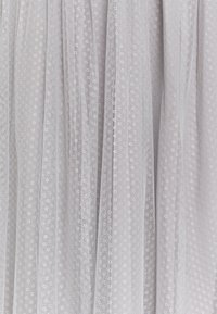 Tejido de tul blanco con un delicado patrón de puntos y pequeños detalles circulares. Textura suave, ligeramente transparente, con un aspecto caído.