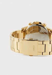 Guldtonet metal armbåndsur med ledetarmen, der har en poleret finish, et rundt urkasse og synlige hardware accenter.