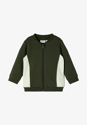 Zielona kurtka na zamek wykonana z miękkiej tkaniny, z białym, prążkowanym bocznym panelem i zaokrąglonym dekoltem. Długie rękawy z prążkowanymi mankietami.