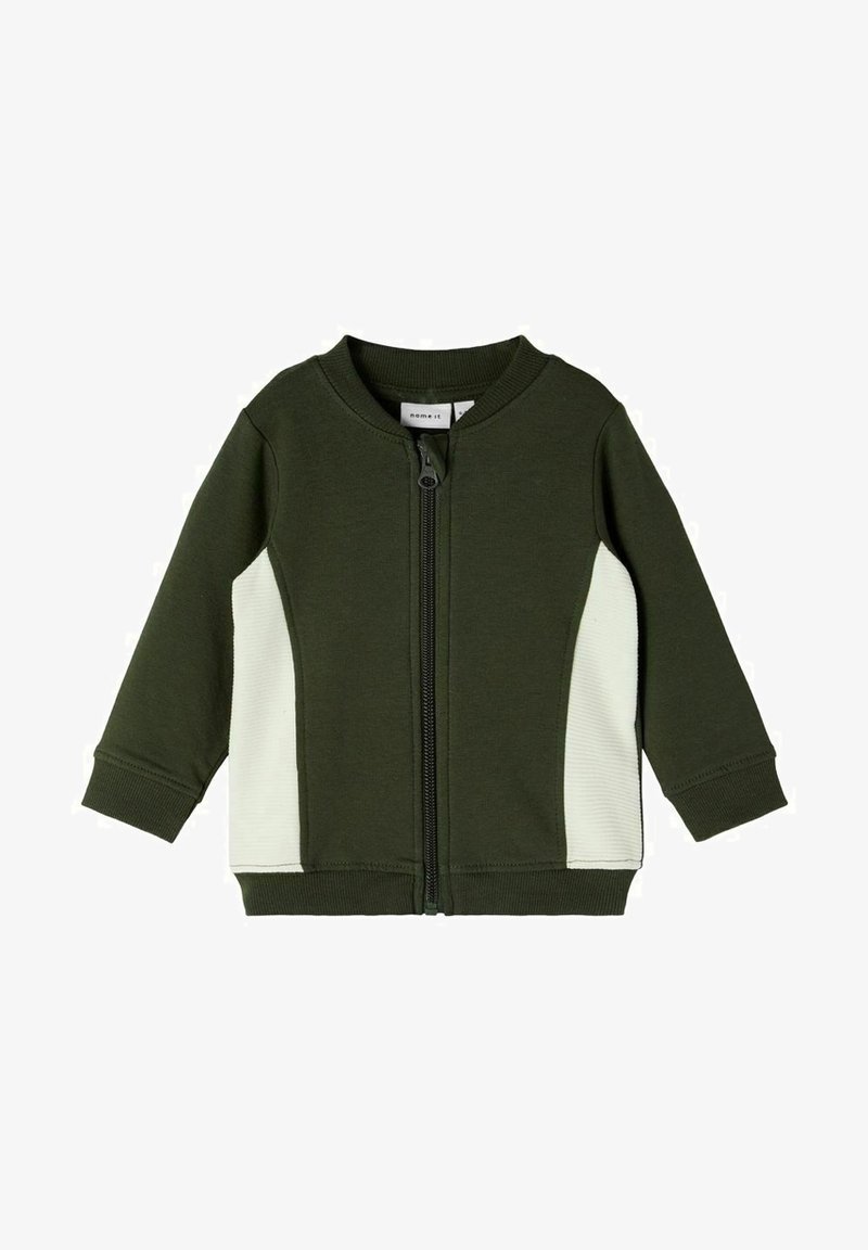 Veste verte à fermeture éclair, en tissu doux, avec un panneau latéral côtelé blanc et un col arrondi. Manches longues avec poignets côtelés.