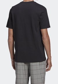 Černé tričko s krátkým rukávem vyrobené z hladké bavlny, s kulatým výstřihem a volným střih, nošené se šedými kostkovanými kalhotami.