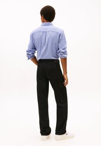 Πουκάμισο με μπλε και λευκές ρίγες και κουμπιά, με τα μανίκια γυρισμένα, συνδυασμένο με μαύρο παντελόνι και λευκά αθλητικά παπούτσια. Απλός, κλασικός σχεδιασμός.