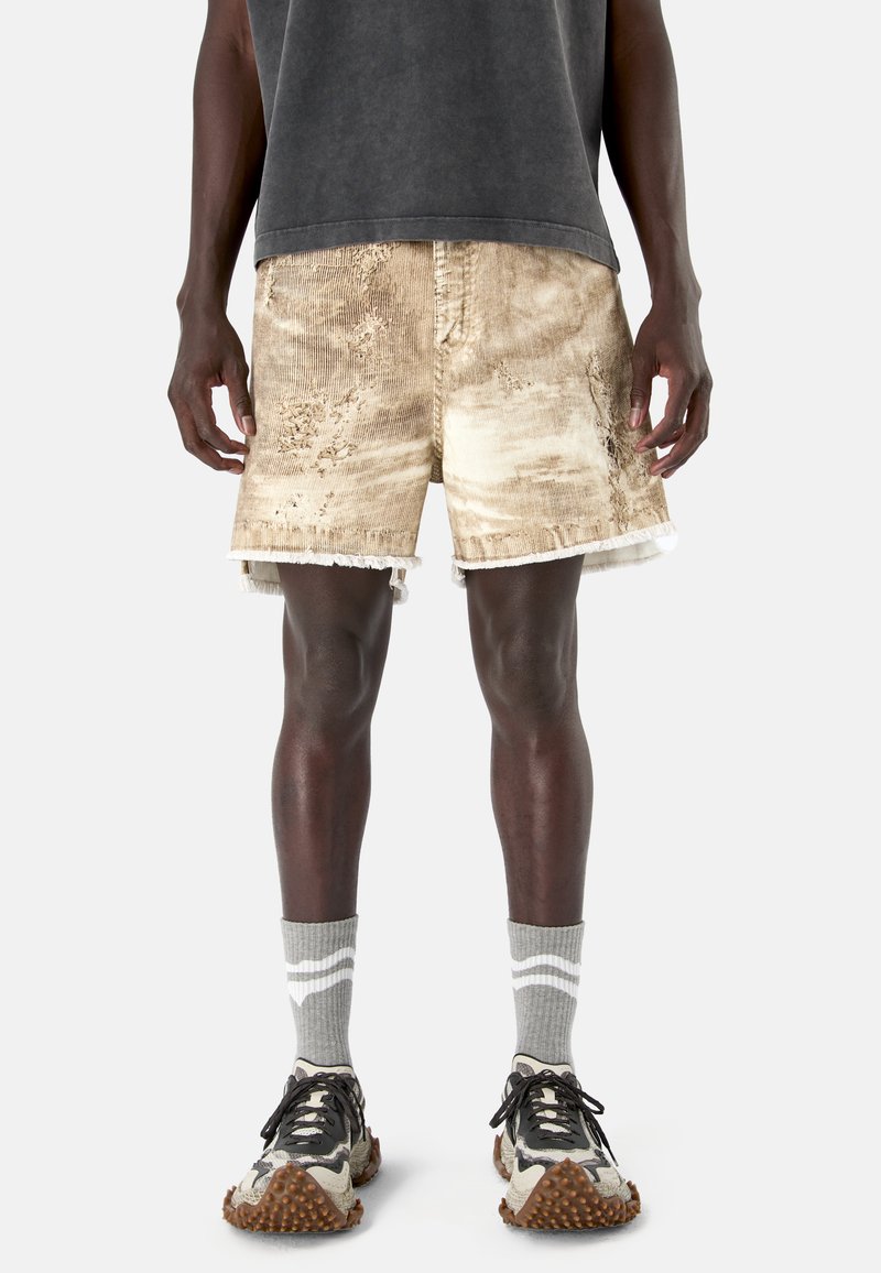 Man wearing distressed beige corduroy shorts, gray crew socks with white stripes, and beige and black textured sneakers.