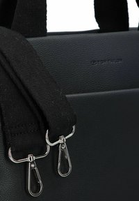 Sac en simili cuir noir avec des anses en tissu noir, arborant des fermoirs en métal argenté et un logo en relief. Surface texturée avec une finition mate.