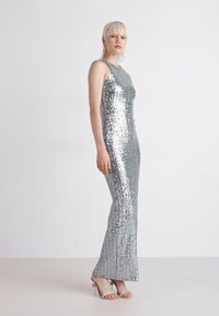 Robe de soirée en sequins argentés avec une silhouette ajustée, design sans manches et ourlet évasé. Associée à des talons argentés à lanières.