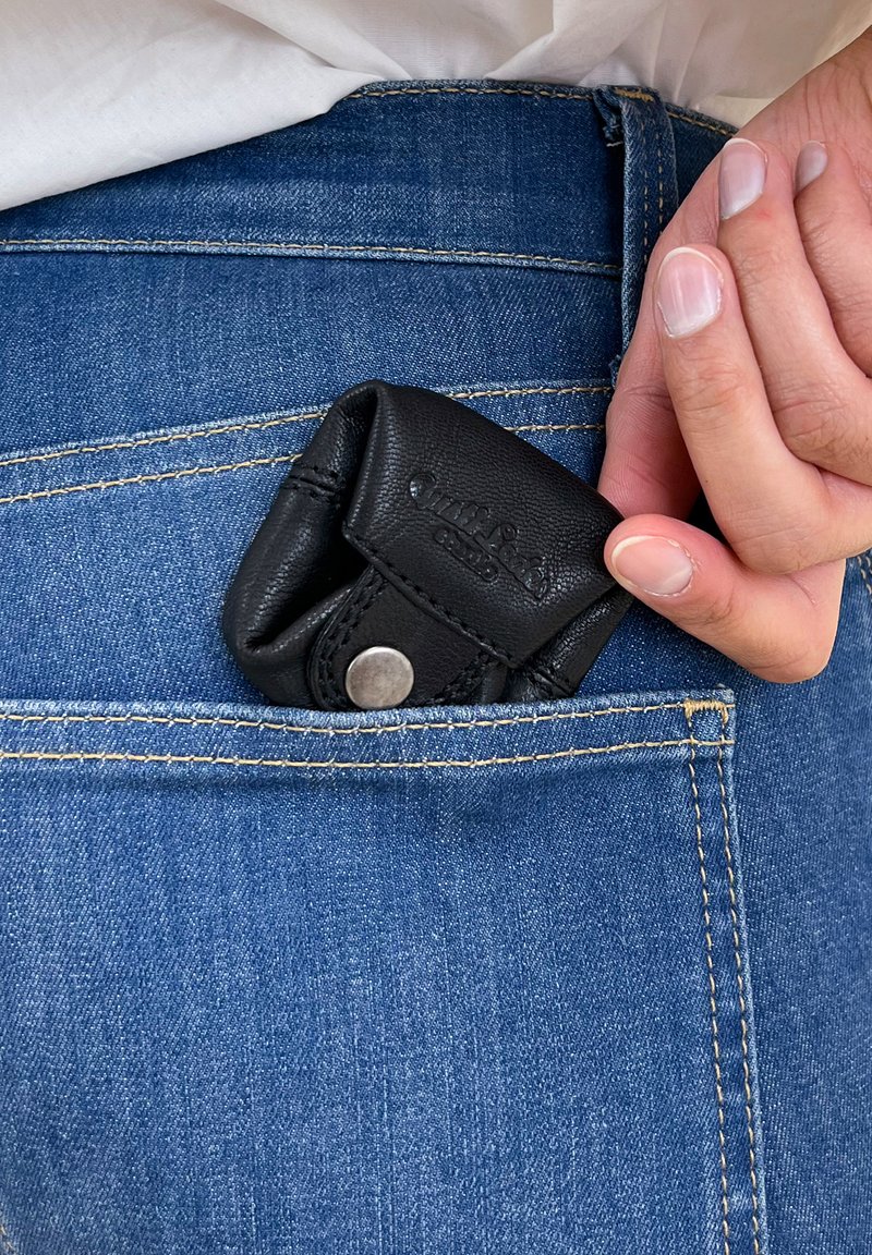Black leather coin pouch partially inserted into the back pocket of blue denim jeans, featuring a snap closure and embossed logo detail.