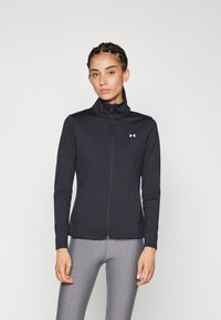 Chaqueta negra con cremallera hecha de un tejido suave, con un cuello alto y un diseño ajustado; incluye un pequeño logo blanco en el pecho.