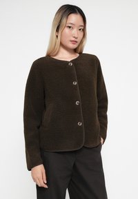 Brown fleece jacket with a round neckline, front button closure, and side pockets, featuring a soft texture and contrasting trim.