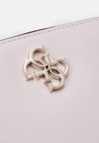 Světle růžová kožená peněženka s lesklým stříbrným kovovým logem. Hladký povrch s zipovým uzávěrem a jemnými švy.