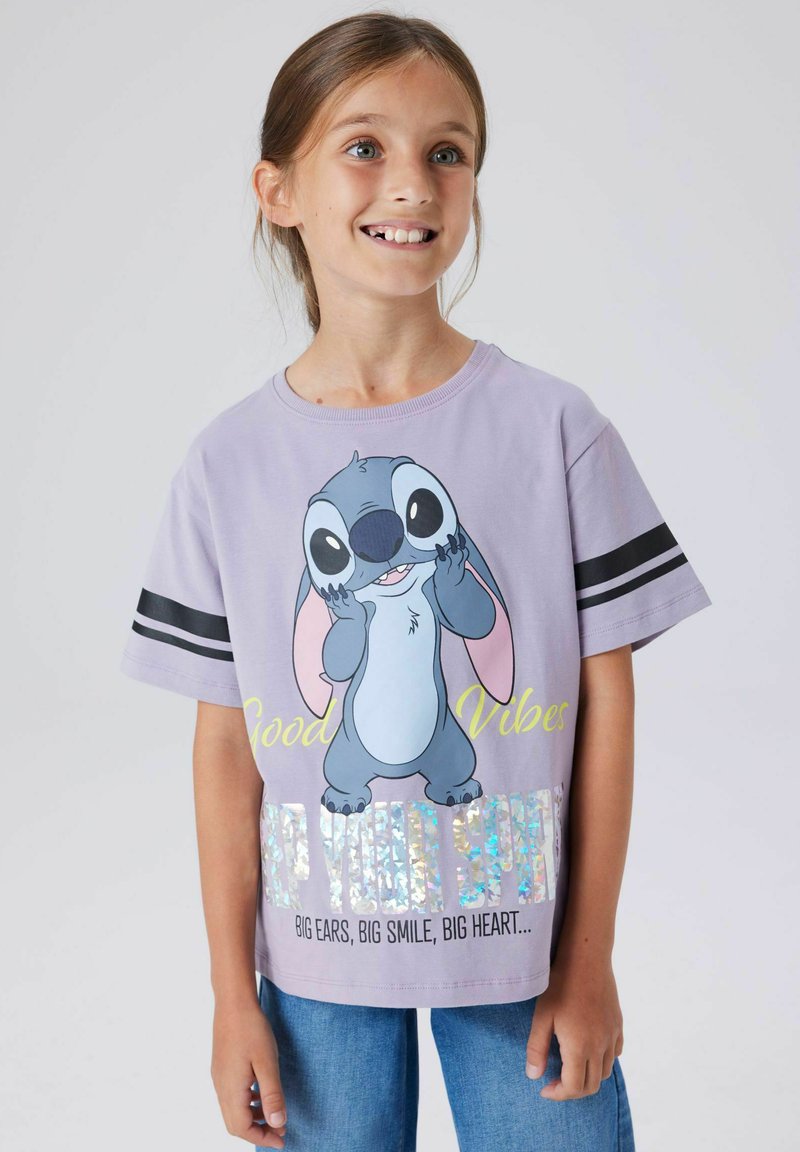 Purple t-shirt featuring a cartoon character with large ears and a smiling expression. Includes black stripes on sleeves and shiny text accents.